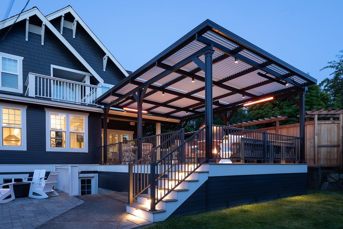 Backyard deck with pergola attached to a dark blue house. Stairs with lights lead up to the deck.