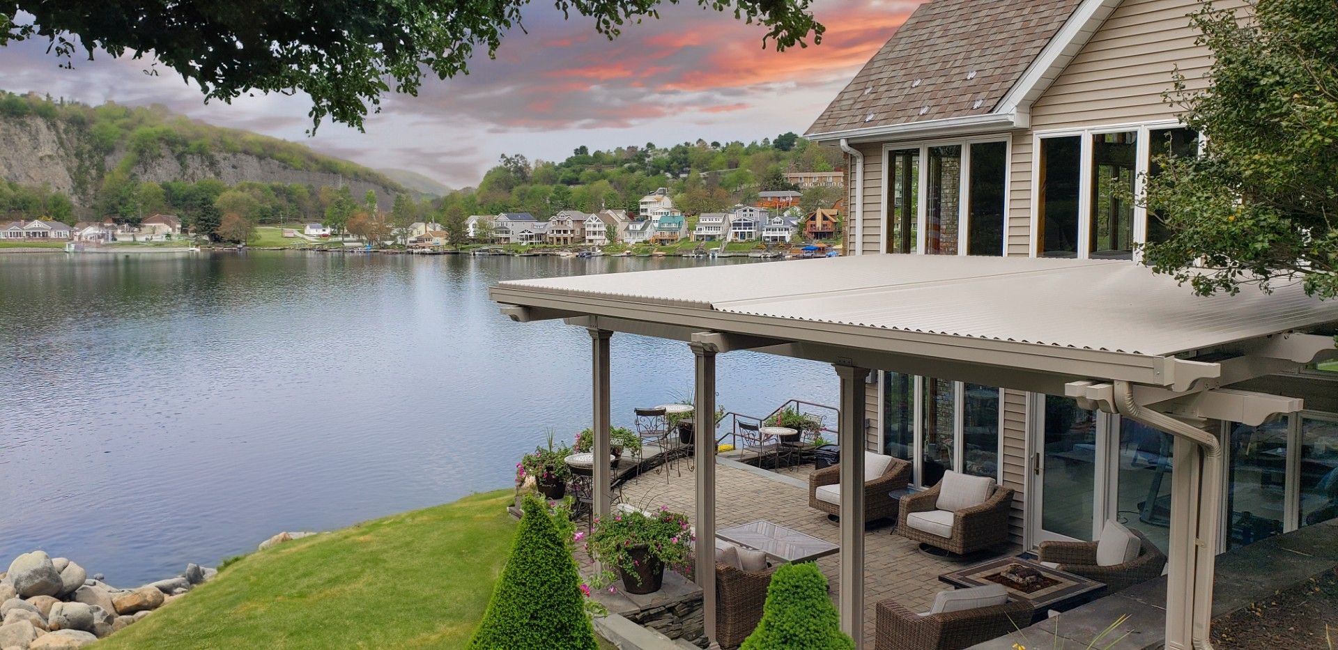 House with lake view; outdoor seating on patio; sunset sky.