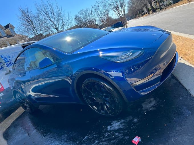 Blue Tesla Model Y car parked on a sunny day; tires are black.