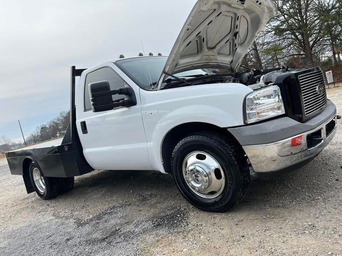 White Ford flatbed truck with the hood open, on gravel.