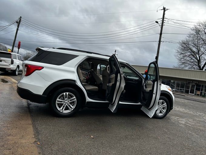 White SUV with open doors parked on a street. The sky is overcast, and the setting appears to be urban.
