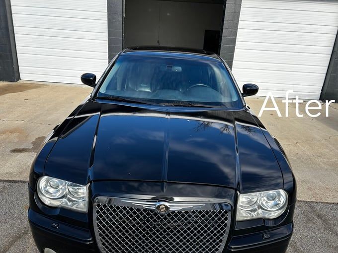 Shiny black Chrysler 300 after detailing, reflecting the sky, parked in front of a garage.