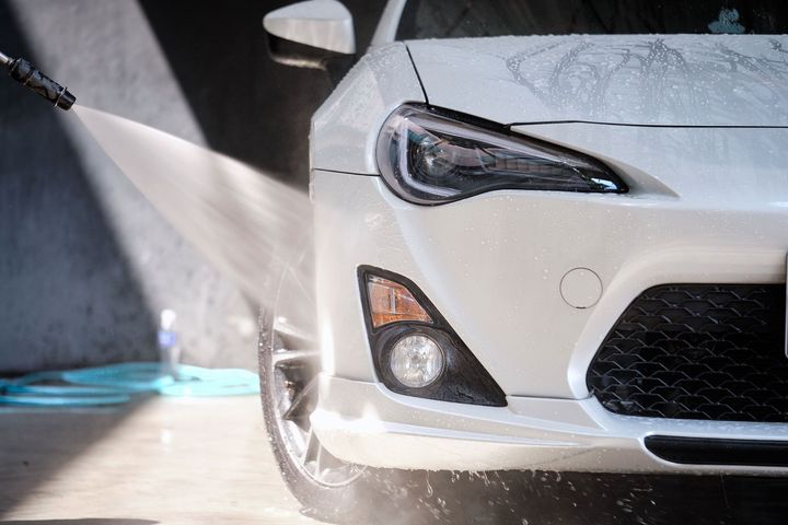 White car being washed with a high-pressure hose, outdoors.
