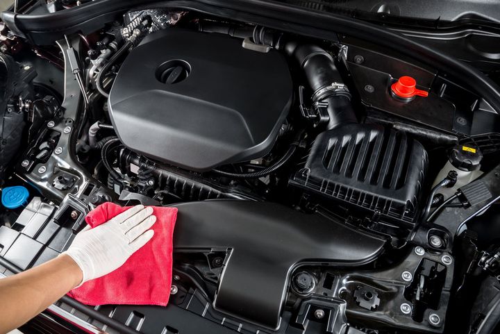 Person wearing white gloves cleaning a car engine with a red cloth.