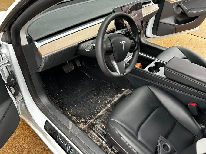 Dirty Tesla Model 3 interior: Black leather seats, steering wheel, and console. Muddy floor mats.