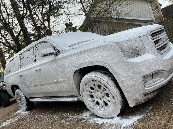 White SUV covered in white foam, outdoors during car wash.