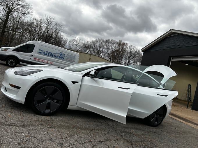 White Tesla with open doors parked outside a building with a delivery van in the background.