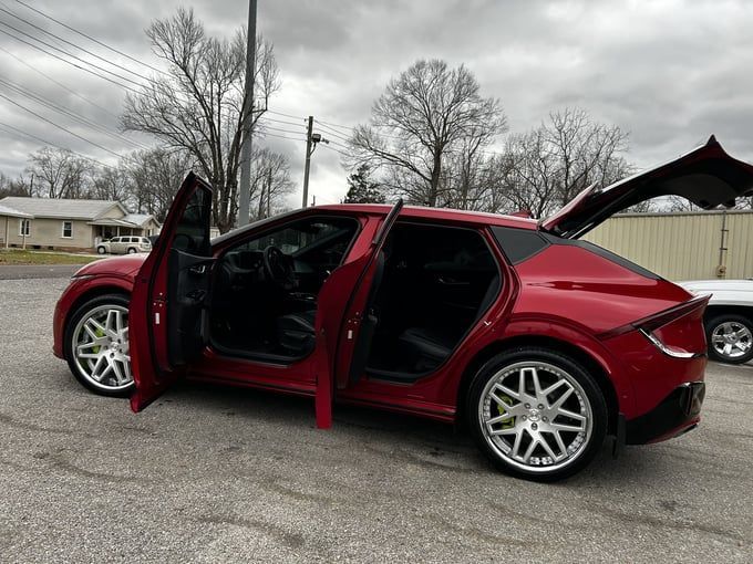 Red Kia EV6 with open doors, parked outdoors on a cloudy day.