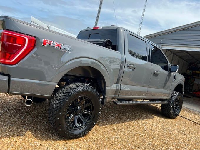 Gray Ford F-150 pickup truck with black wheels and FX4 badging parked outside a garage.