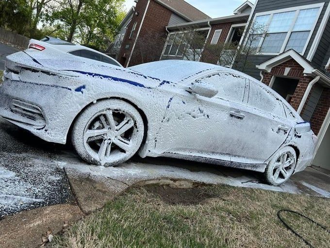 White car covered in white foam, being washed on a driveway.