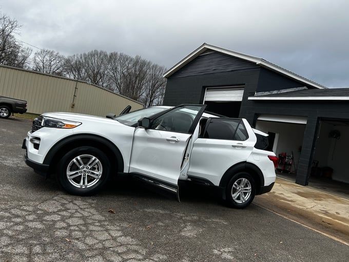 White Ford Explorer SUV parked with doors open near a black building with garage doors.