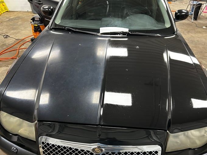 Car hood, half dull and half polished, reflecting lights. Black paint.