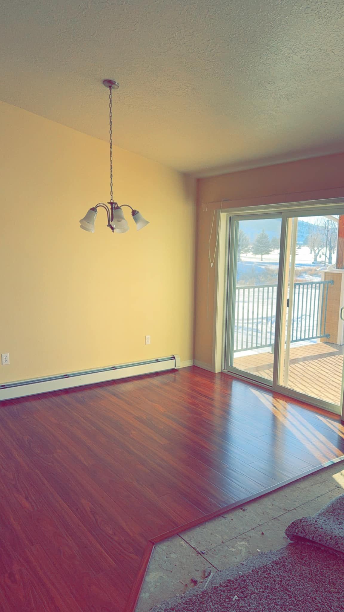 An empty living room with hardwood floors and a chandelier hanging from the ceiling.