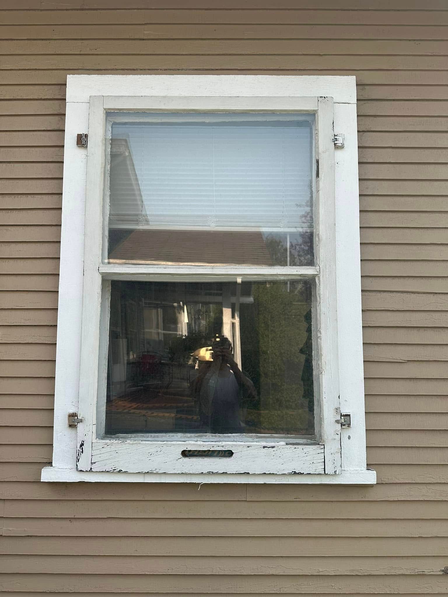 A window on the side of a house with a reflection of a person in the window.