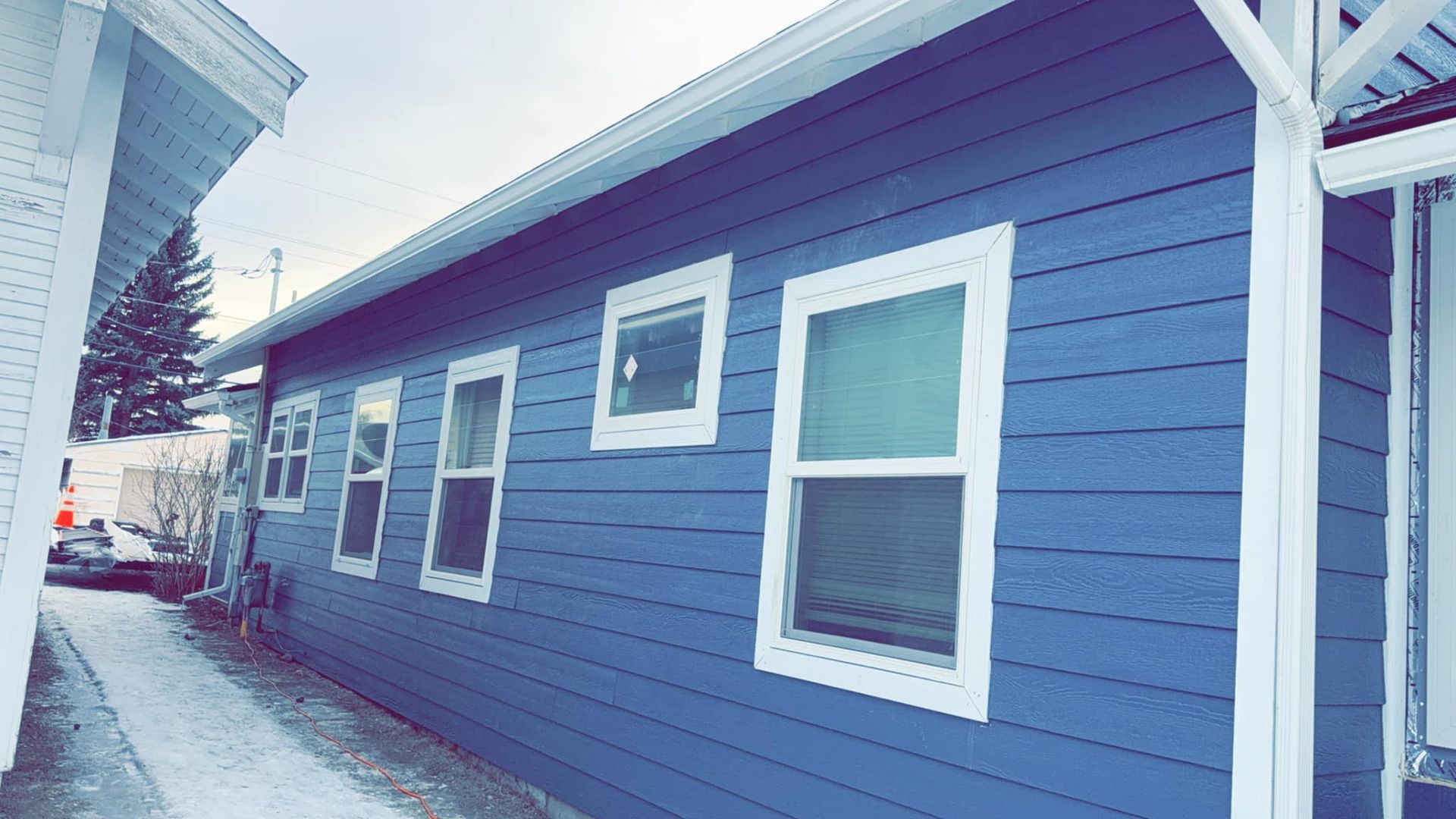 A blue house with white trim and windows on a snowy day.