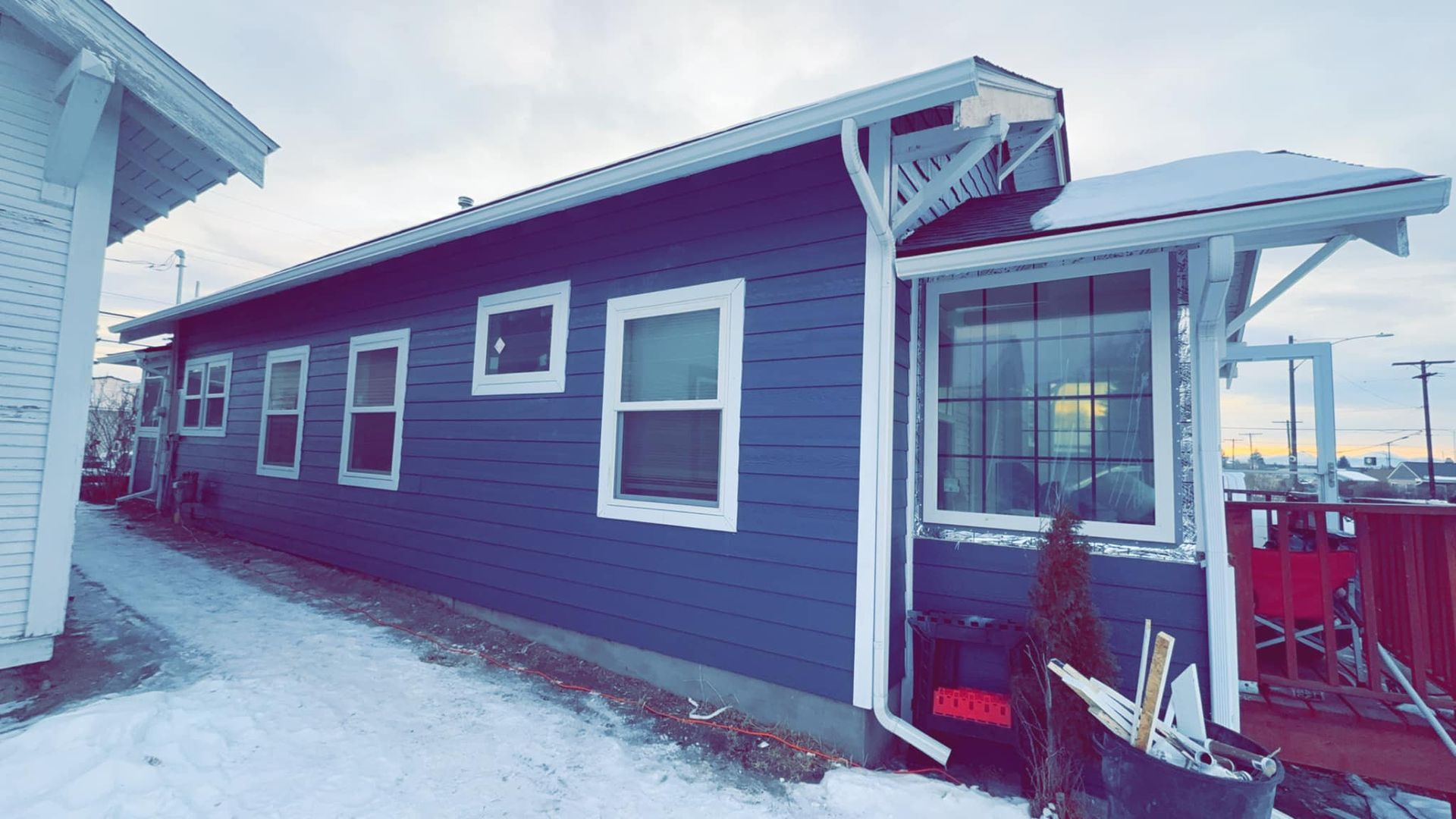 A blue house with white windows is covered in snow.