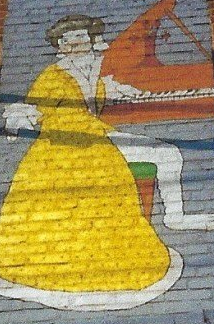 A painting of a woman in a yellow dress on a brick wall