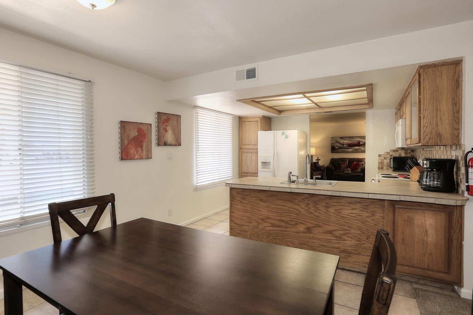 A dining room with a table and chairs and a kitchen in the background.