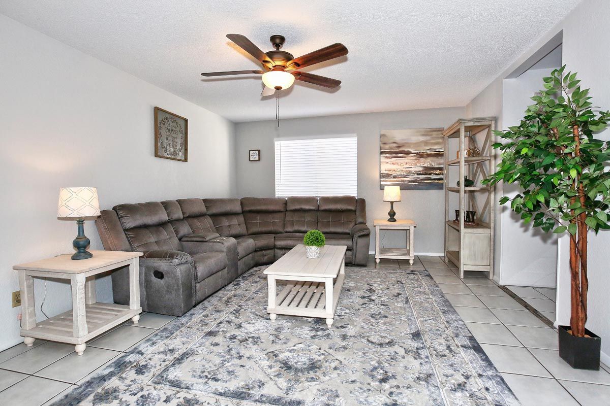 A living room with a sectional couch , coffee table , lamps and a ceiling fan.