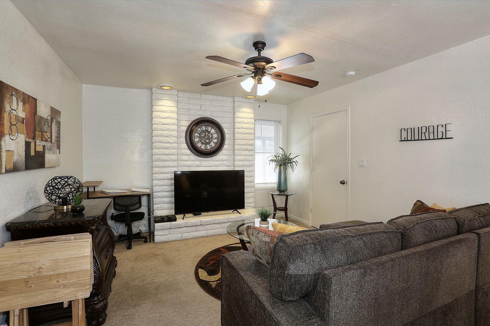 A living room with a couch , television , desk and ceiling fan.