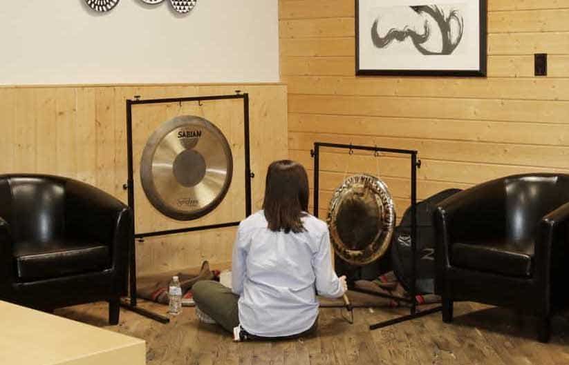 A woman is sitting on the floor playing a gong in a room with chairs.