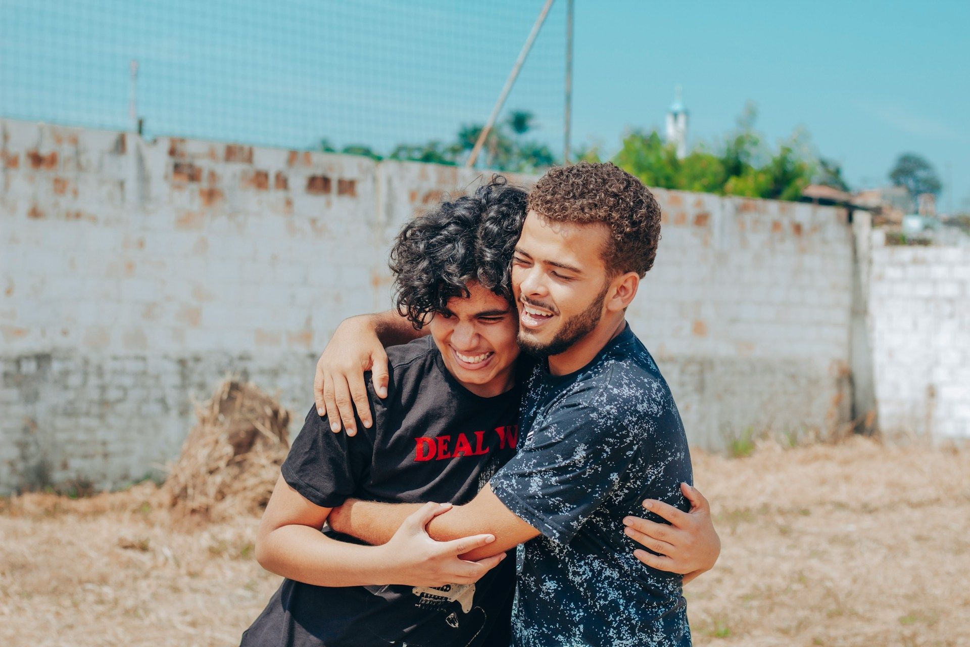 Two young men are hugging each other in a field.