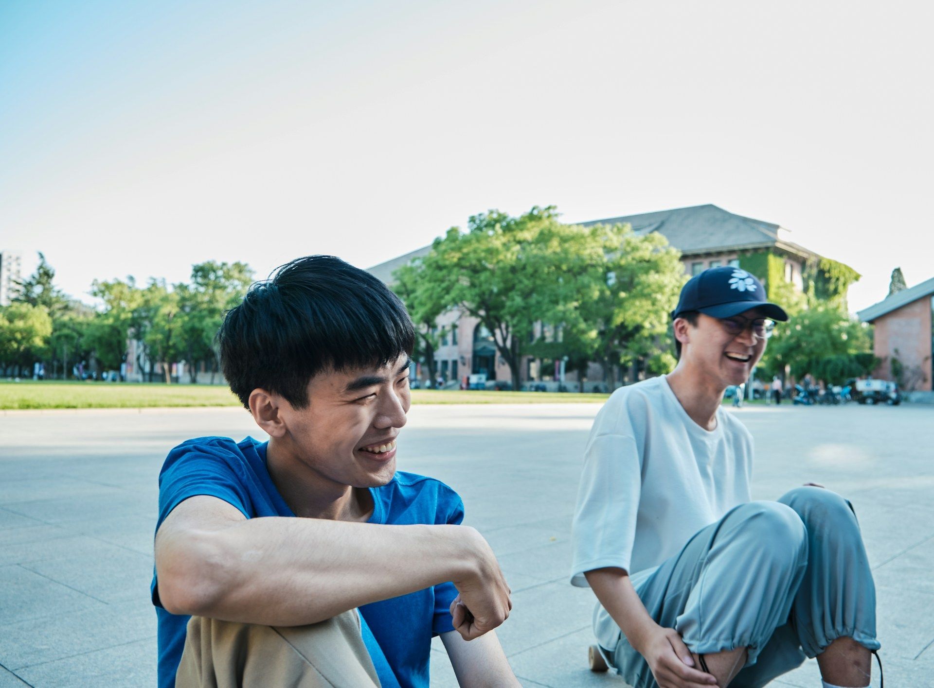 Two young men are sitting next to each other on the sidewalk.