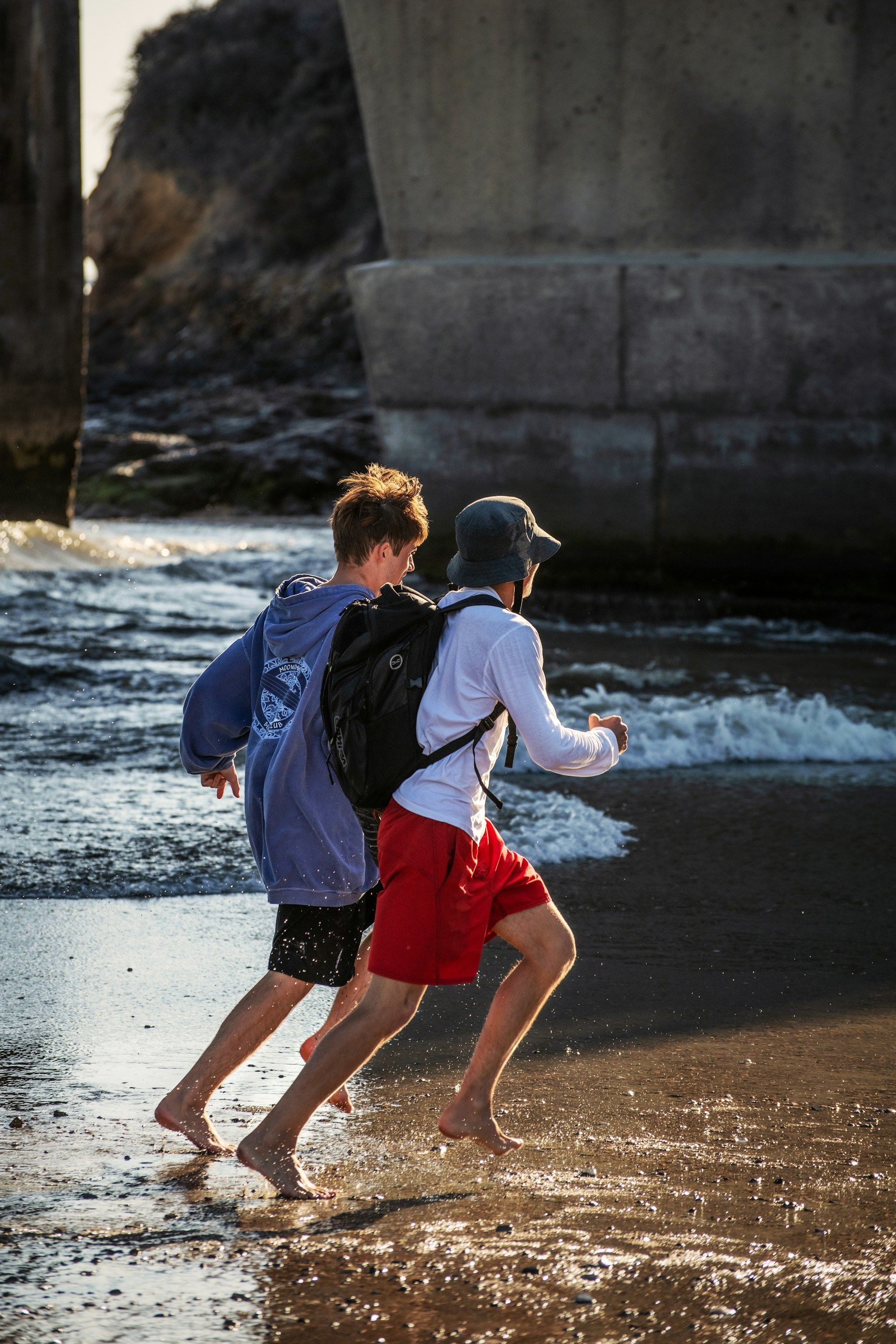 Two boys are running in the water on the beach.