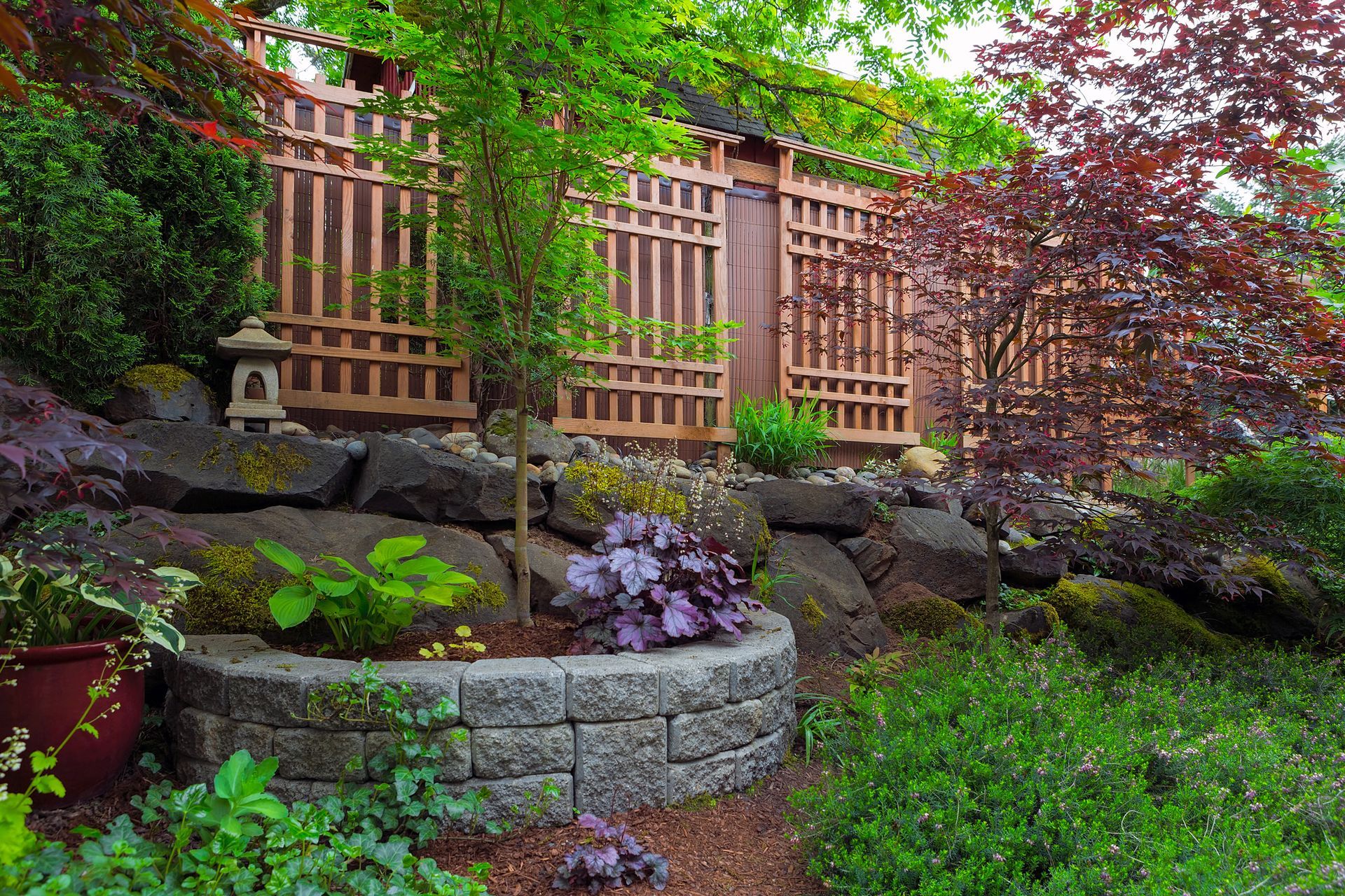Japanese garden with stone planter, lush greenery, and wooden privacy fence.