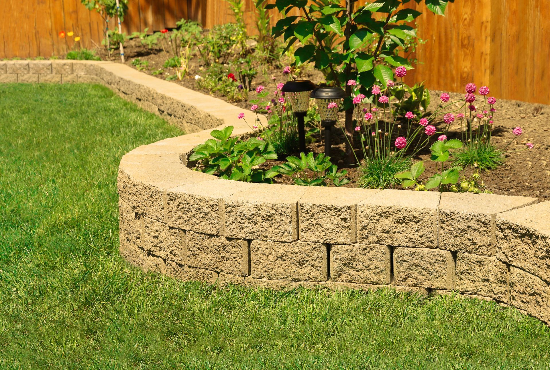 Raised garden bed with flowers and plants bordered by stone blocks.