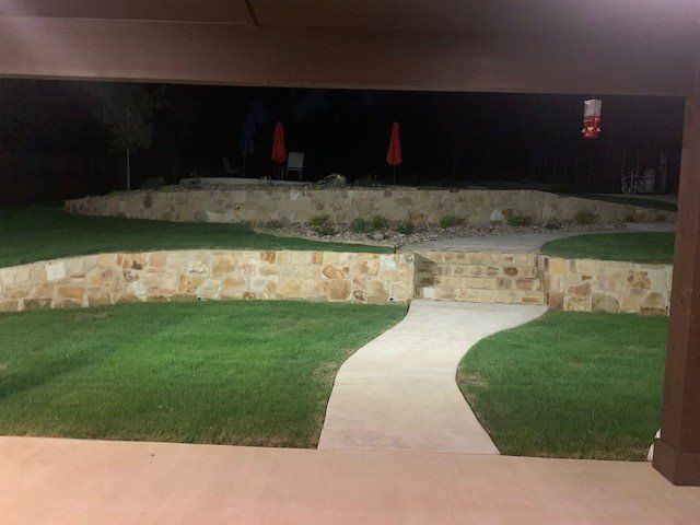 A stone-walled backyard with a green lawn, a winding pathway, and dark sky.