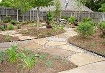 A serene backyard garden featuring a stone path winding through various plants and greenery.