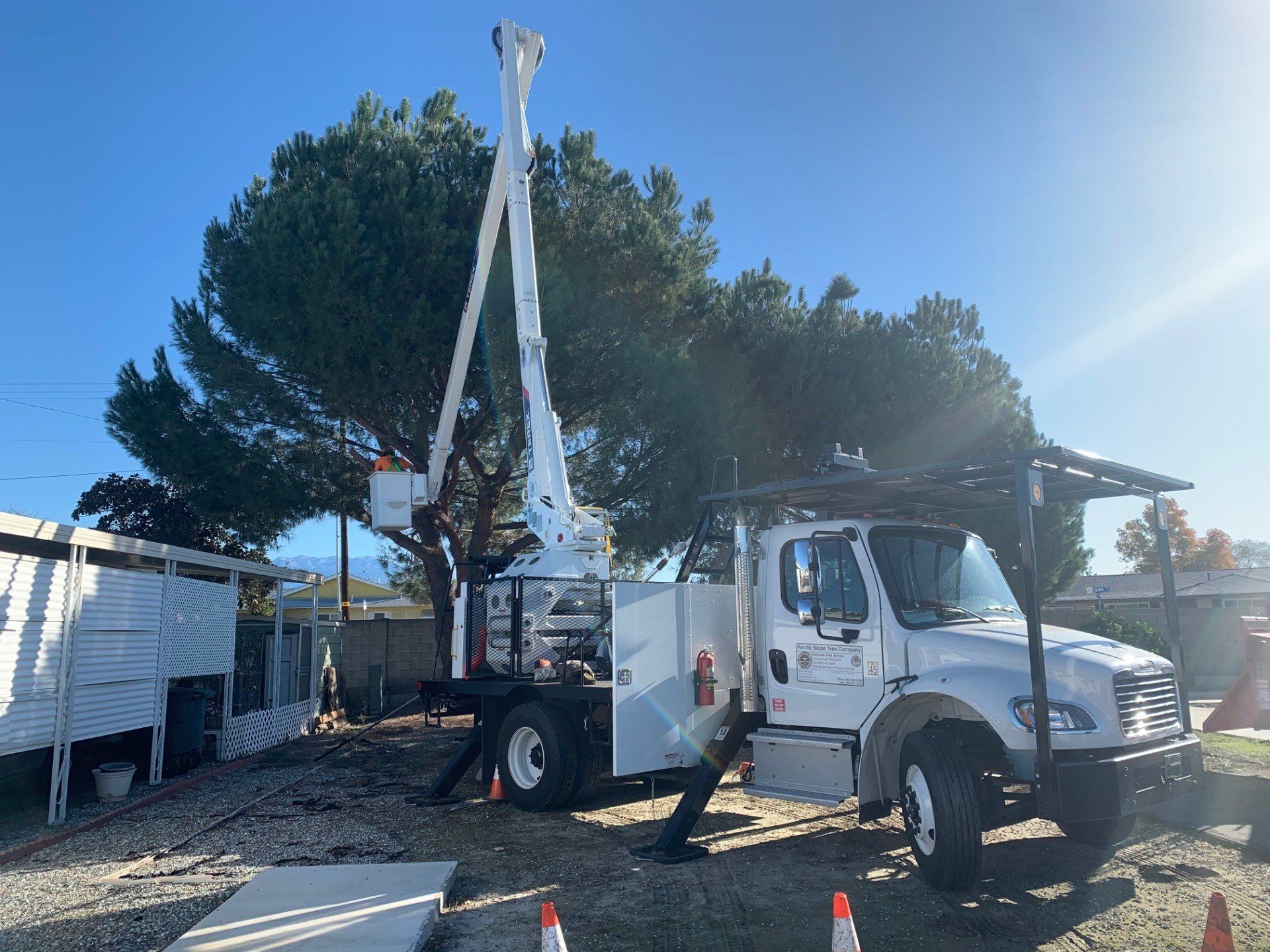 A white truck with a crane on top of it is parked in front of a tree.