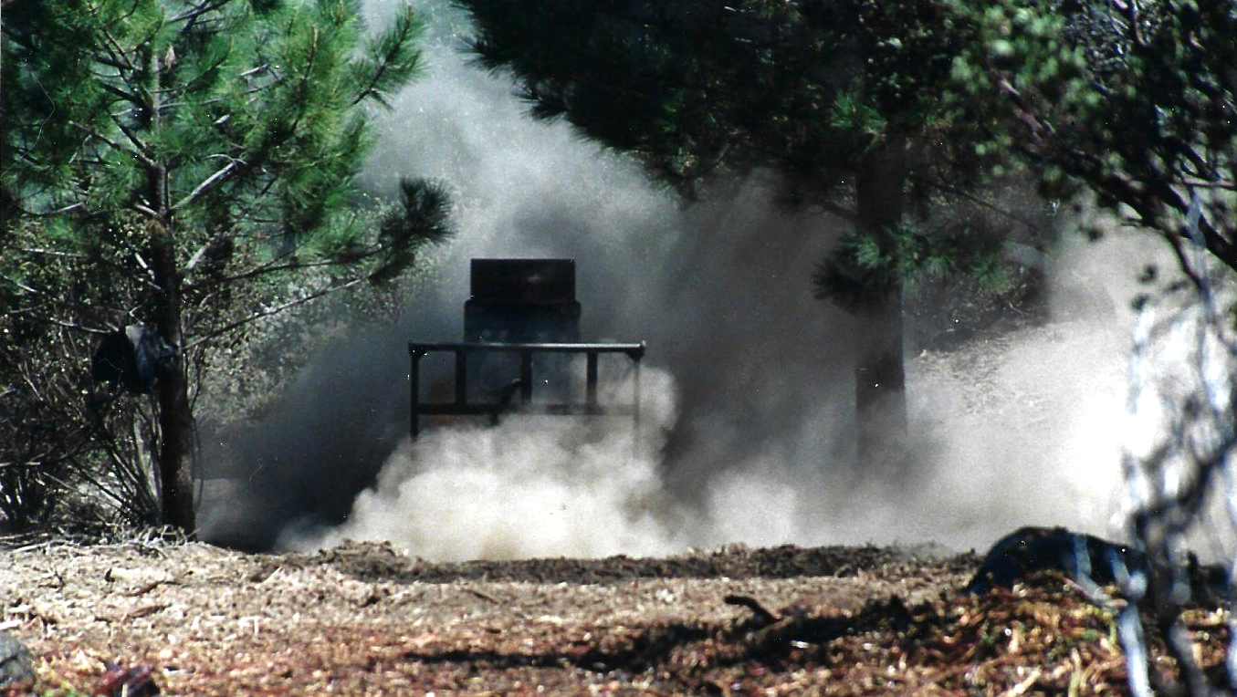 A tractor is driving through a forest with smoke coming out of it.