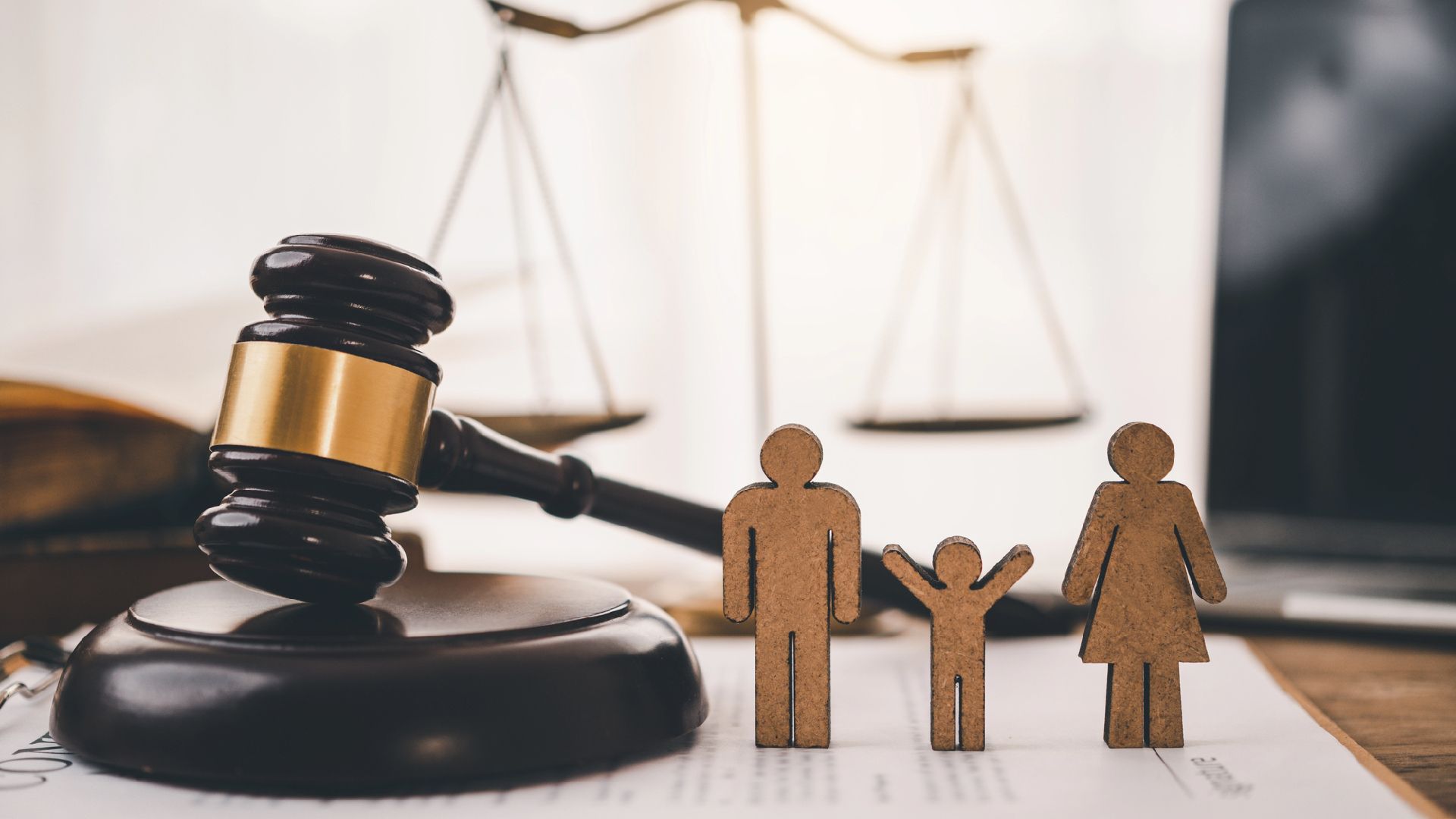 Balanza dorada de la justicia sobre un escritorio, una persona con traje tecleando en un ordenador portátil al fondo.