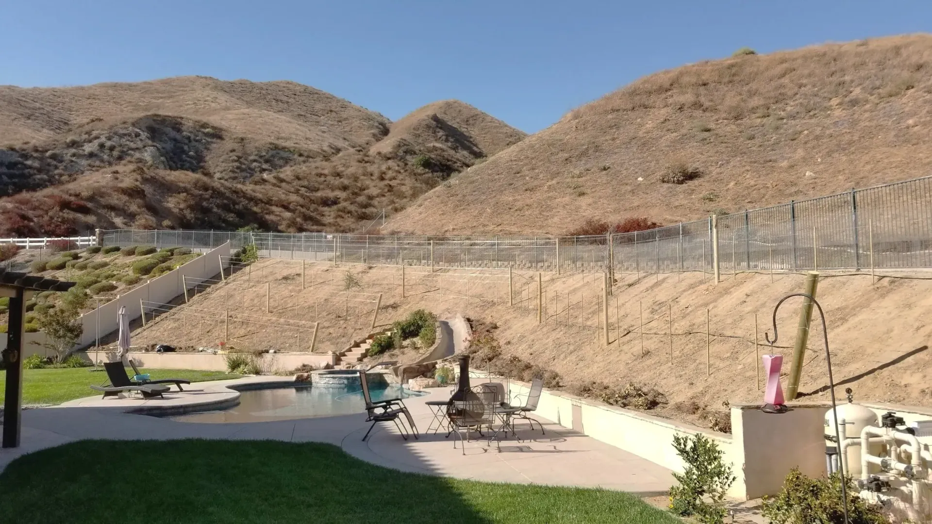 A pool and patio area with mountains in the background. Sunny, outdoor setting.