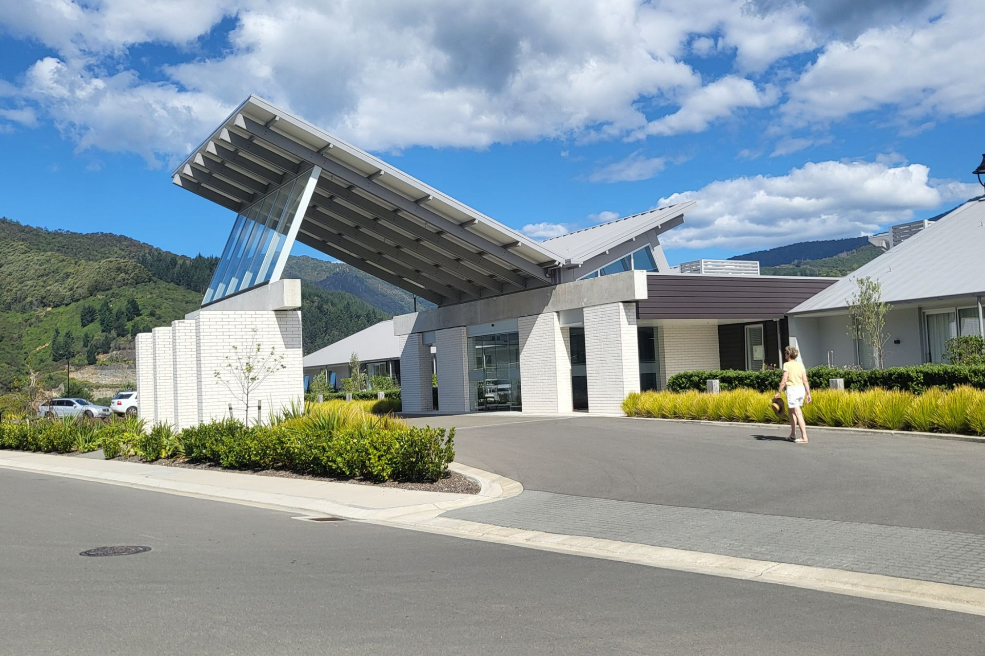 Modern building entrance with angled roof; person walks nearby under blue sky.