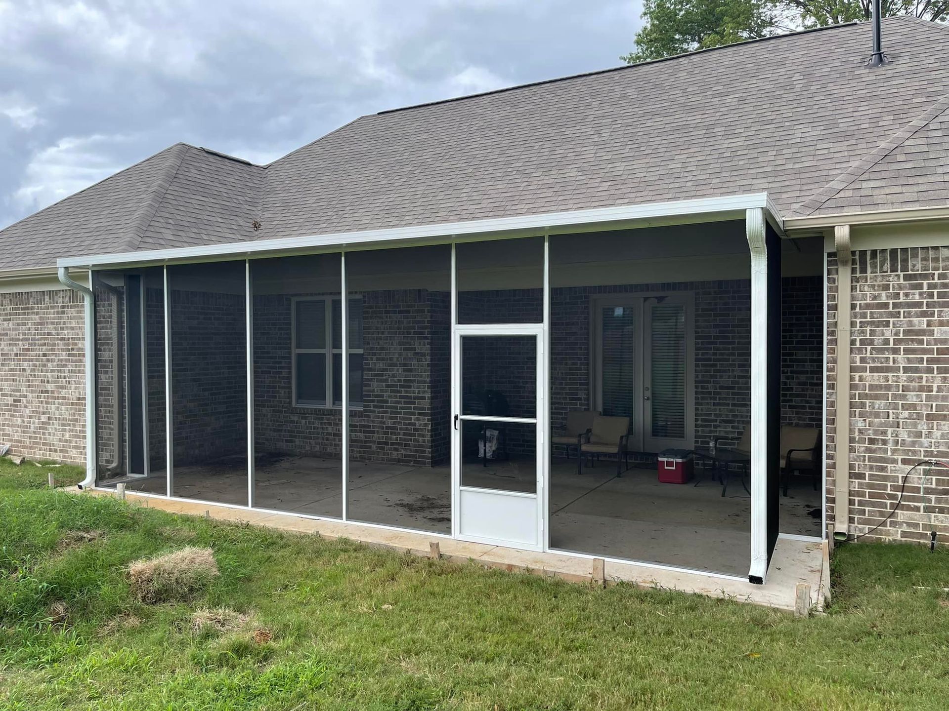 A screened in porch on the side of a brick house.