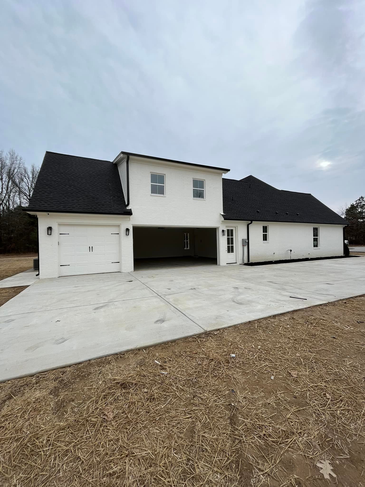 A white house with a black roof is sitting on top of a gravel driveway.