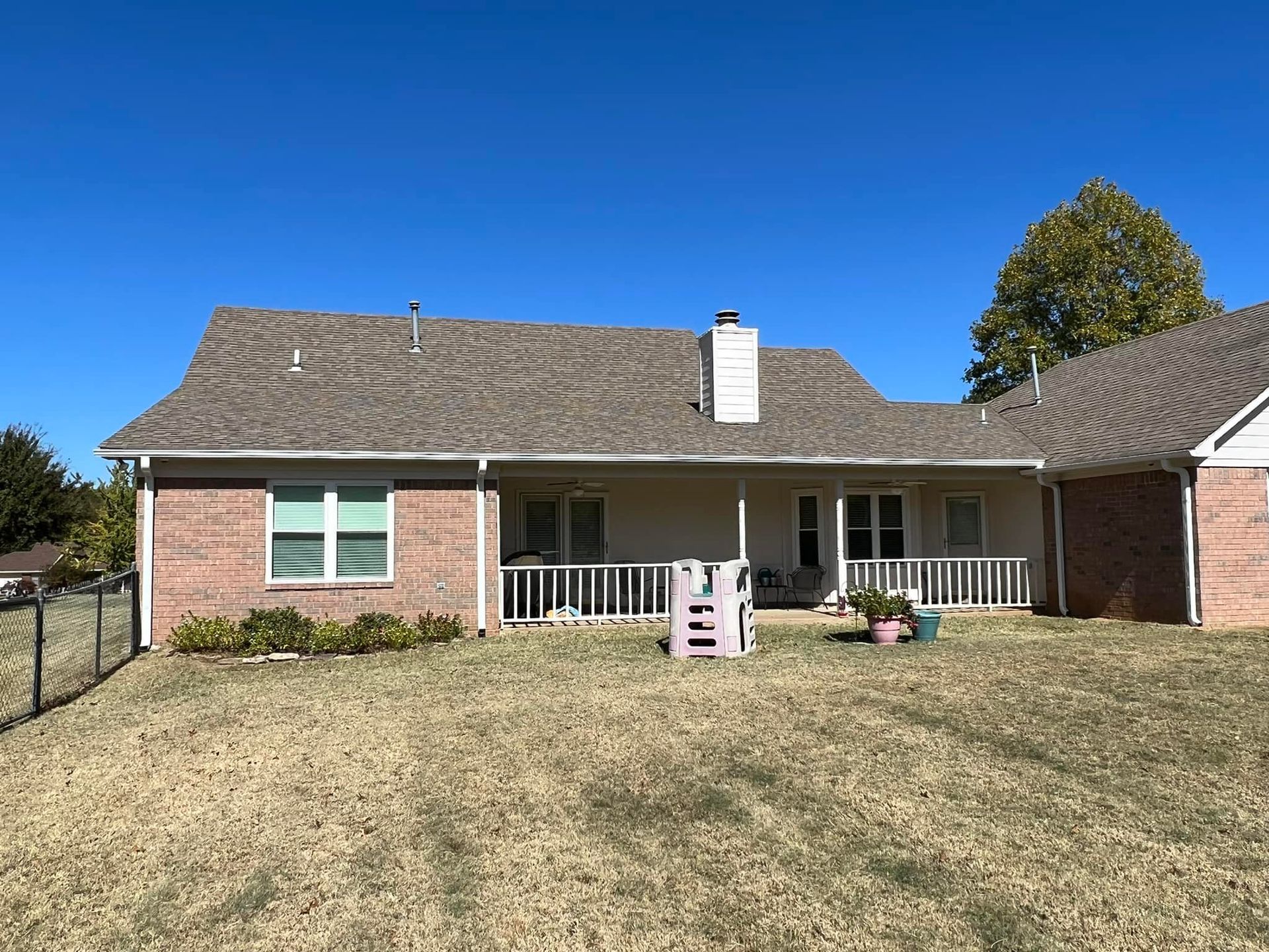 A brick house with a porch and a fence in front of it.