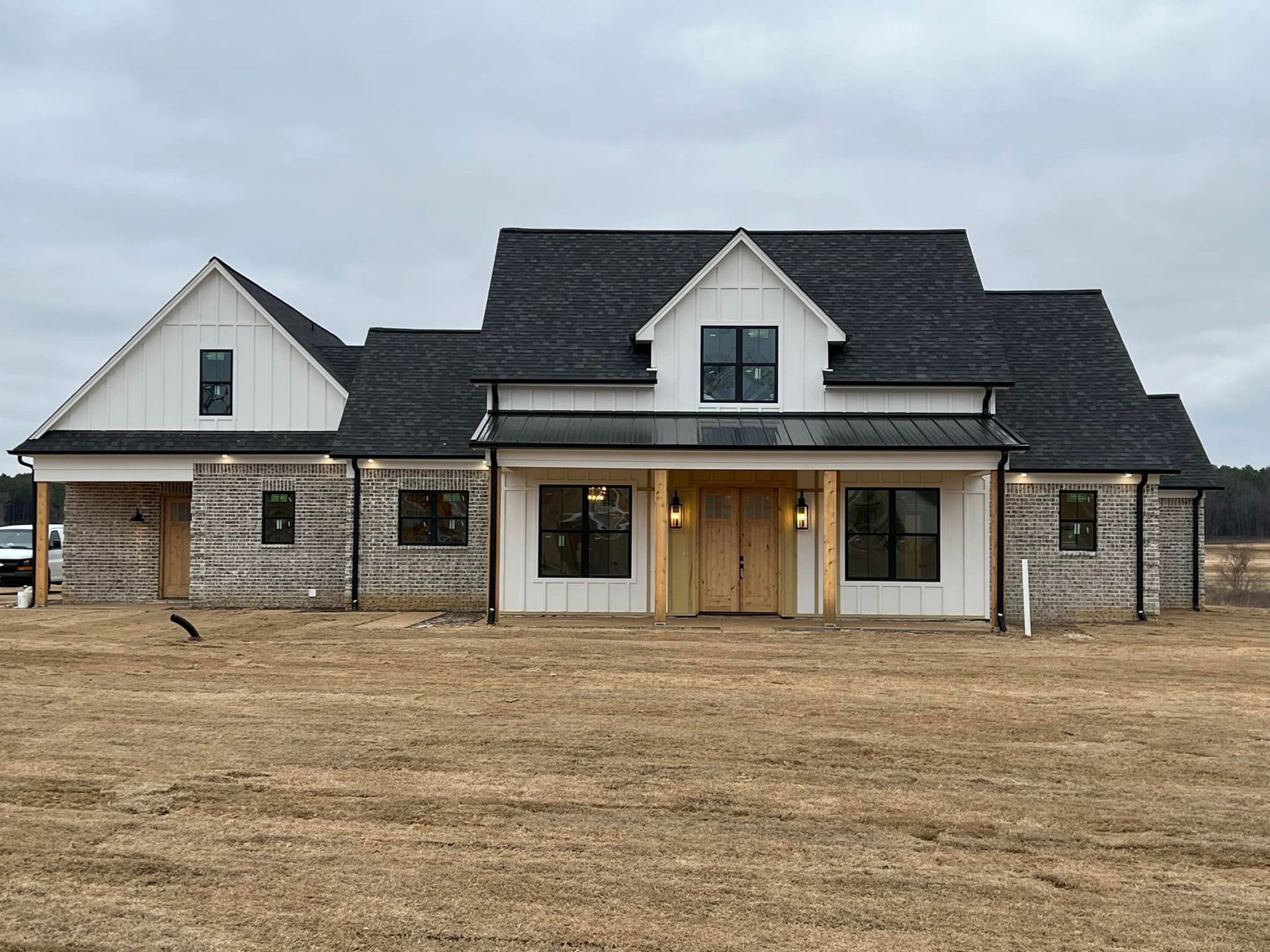 A large white house with a black roof is sitting in the middle of a field.