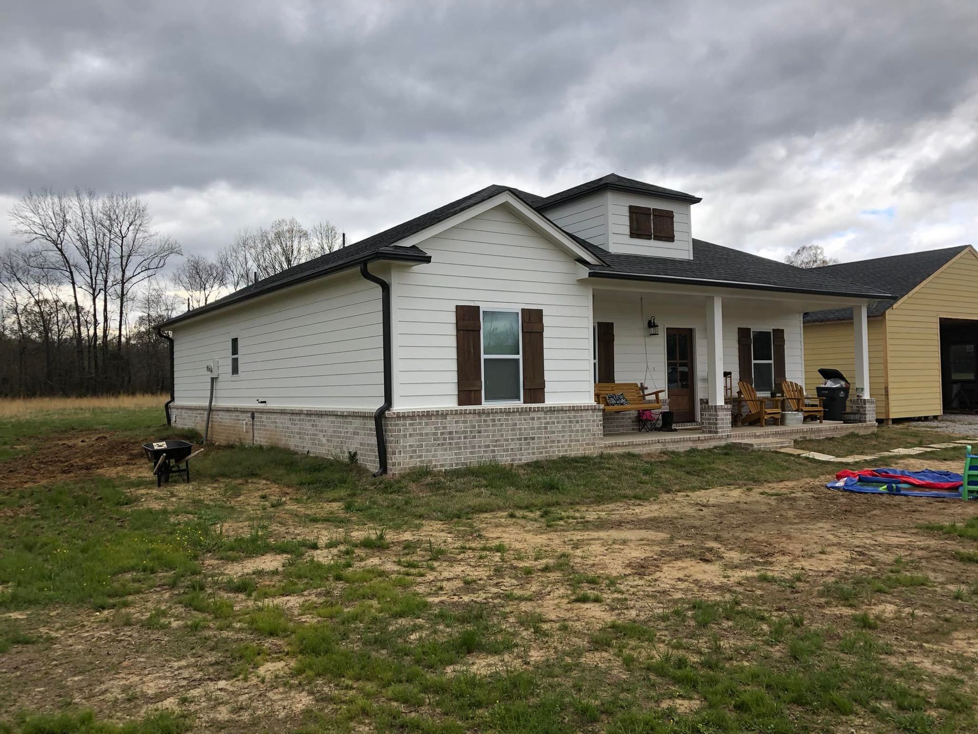 A white house with brown shutters is sitting in the middle of a grassy field.