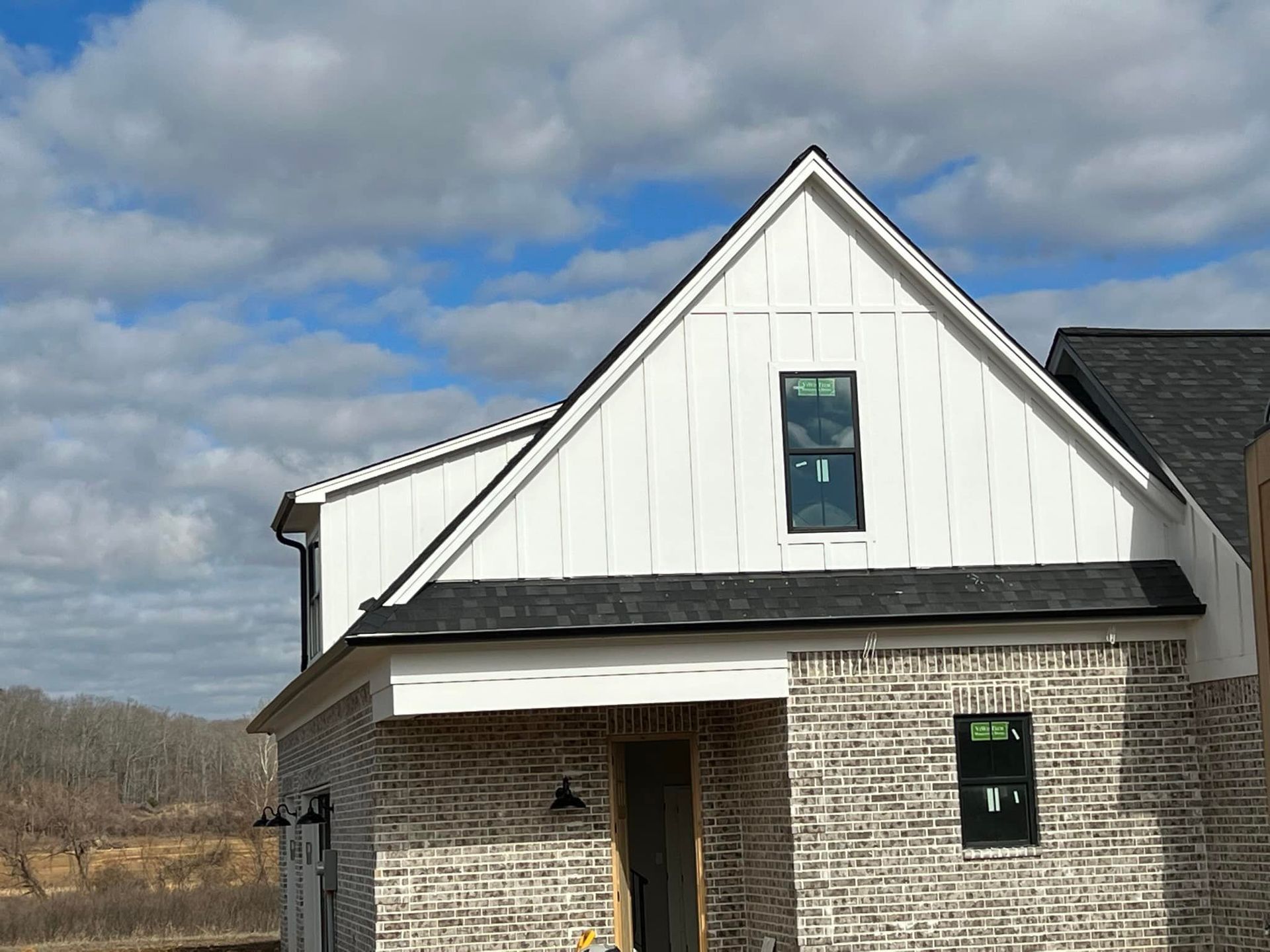 A brick house with a white siding and a black roof is being built.