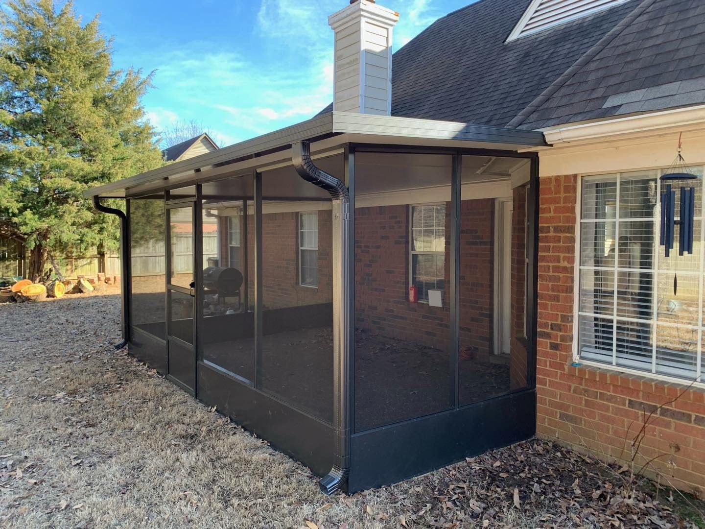 A screened in porch on the side of a brick house.