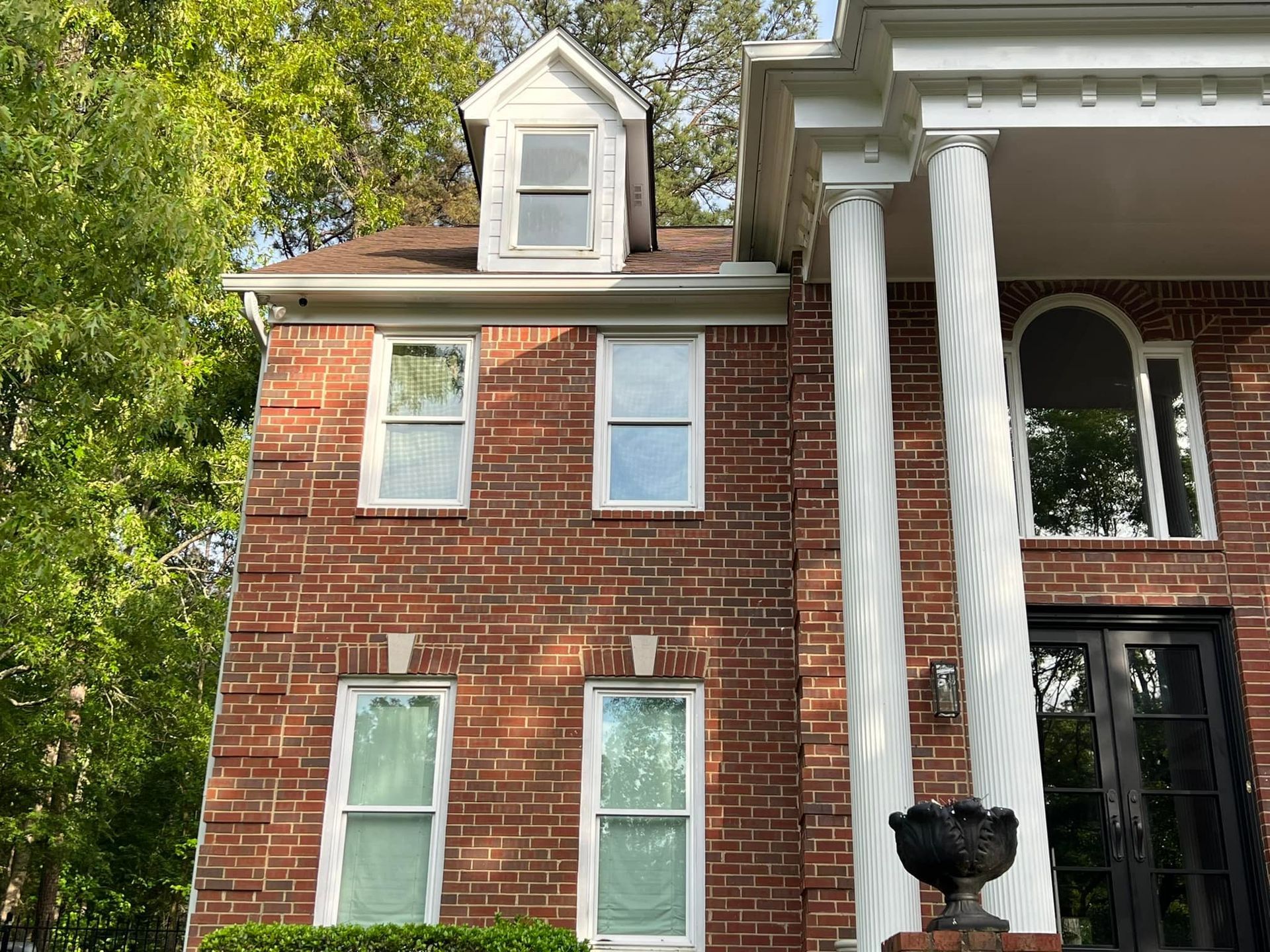 A large brick house with a porch and columns is surrounded by trees.