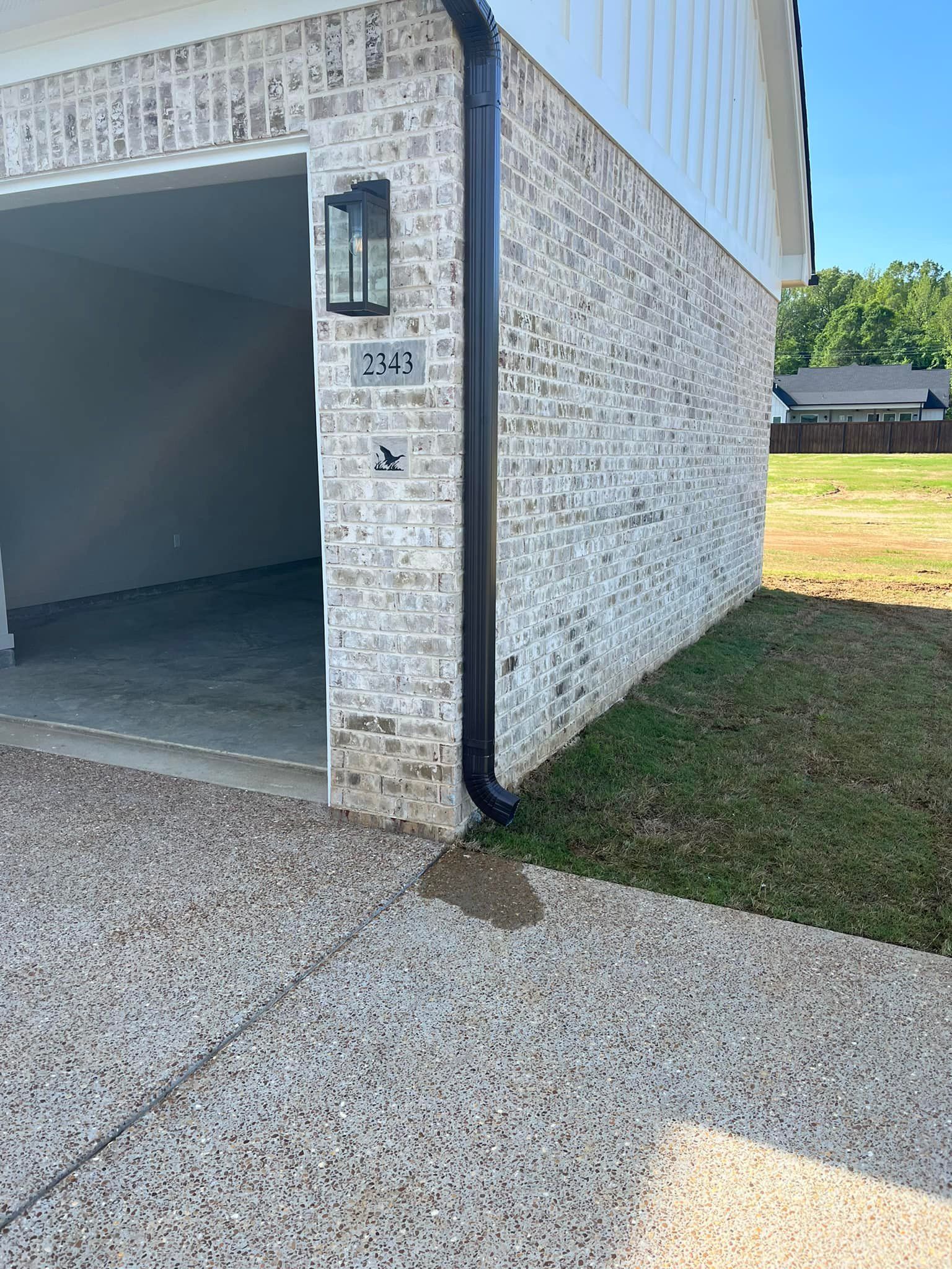A white brick house with a black gutter on the side of it.
