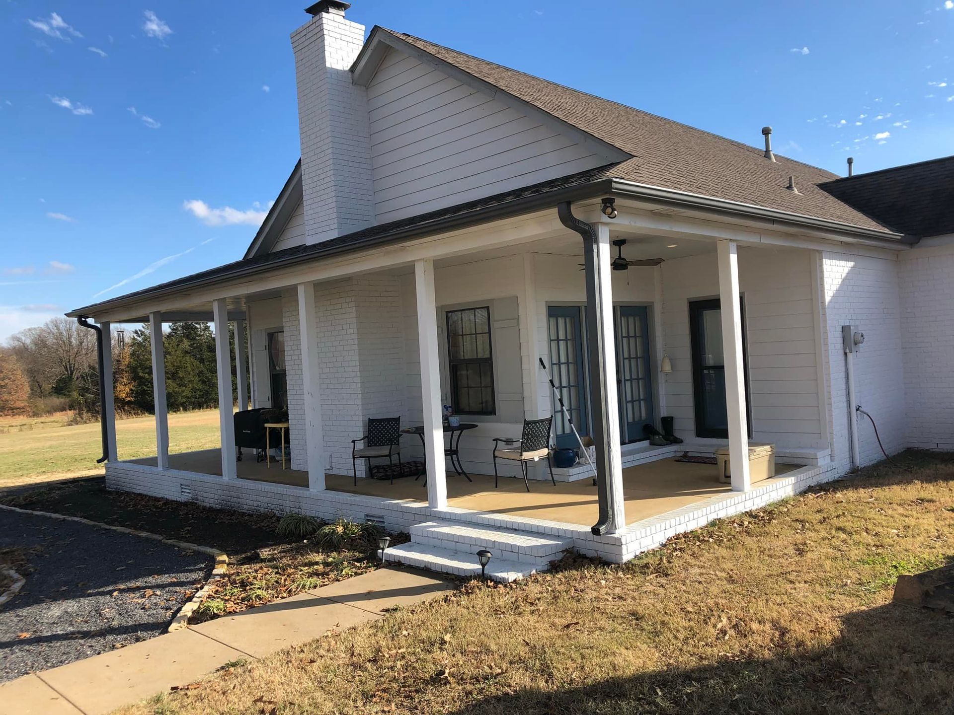 A white house with a porch and a roof on a sunny day.