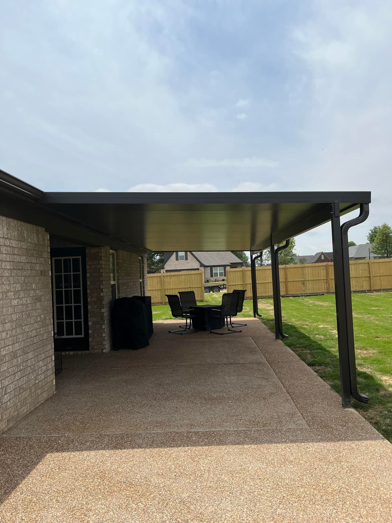 A patio with a table and chairs under a canopy in front of a brick house.
