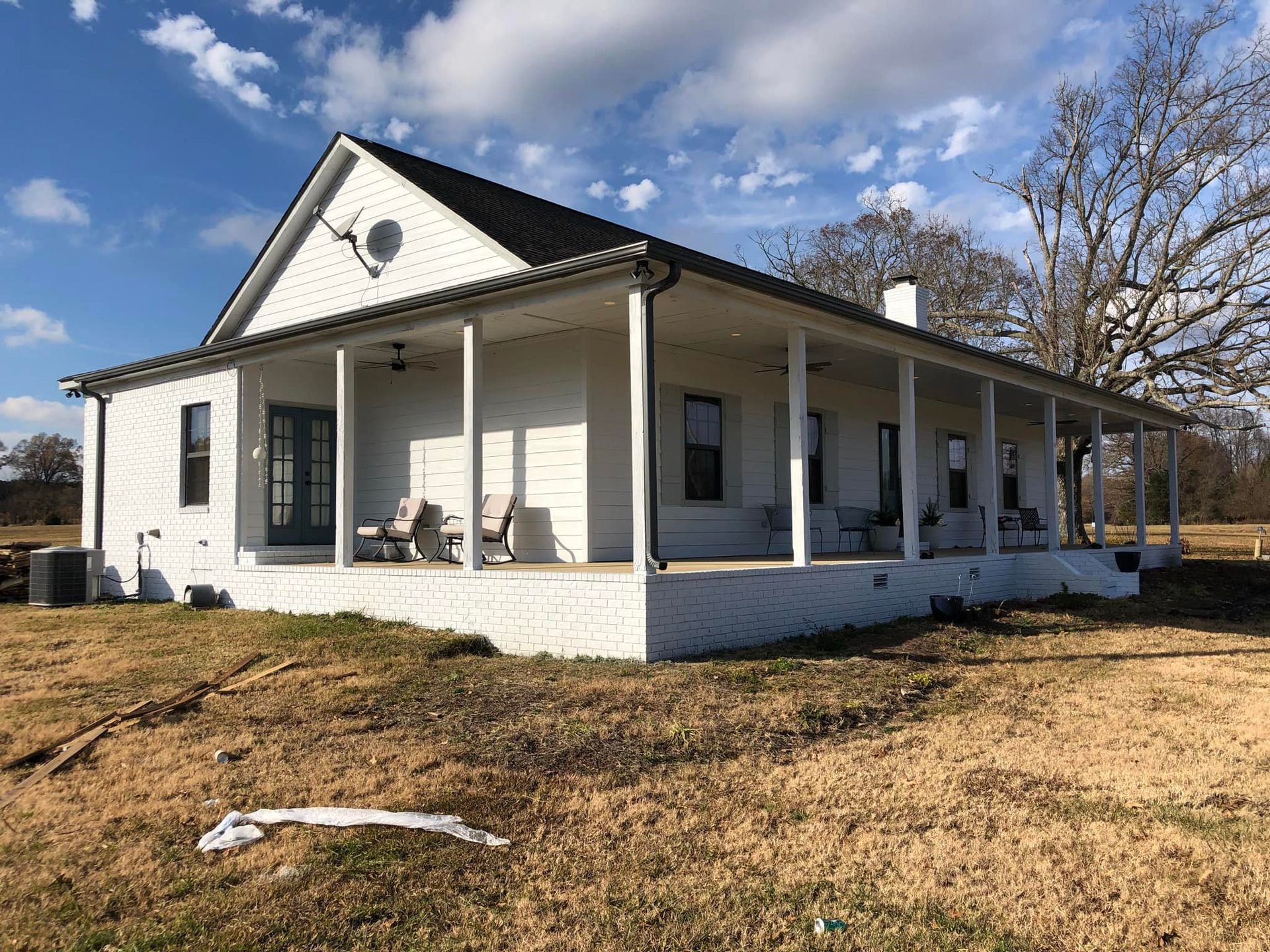 A white house with a porch in the middle of a field.