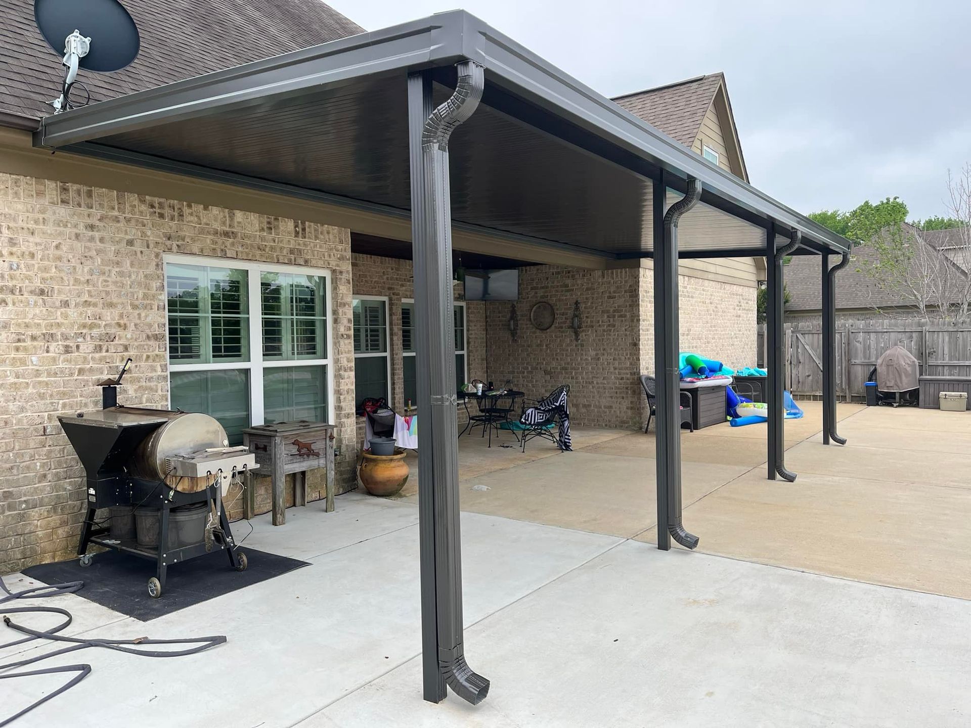 A covered patio with a grill and a satellite dish on the roof of a house.